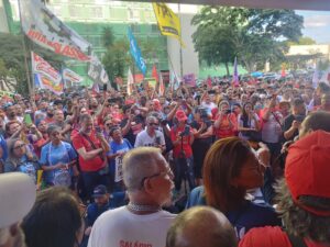 Centenas de pessoas de pé, várias delas segurando bandeiras e cartazes. 