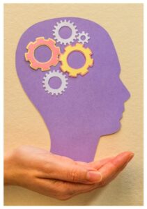 Desenho roxo de uma cabeça de perfil virada para a direita, apoiada sobre a mão de uma pessoa de pele branca. Dentro da cabeça, na região do crânio, há desenhos de engrenagens de diferentes tamanhos e cores. 