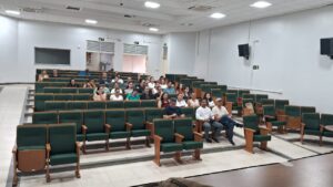 Cadeiras do auditório vistas de frente. Um pequeno número de pessoas ocupa as cadeiras mais centrais, junto do corredor. 