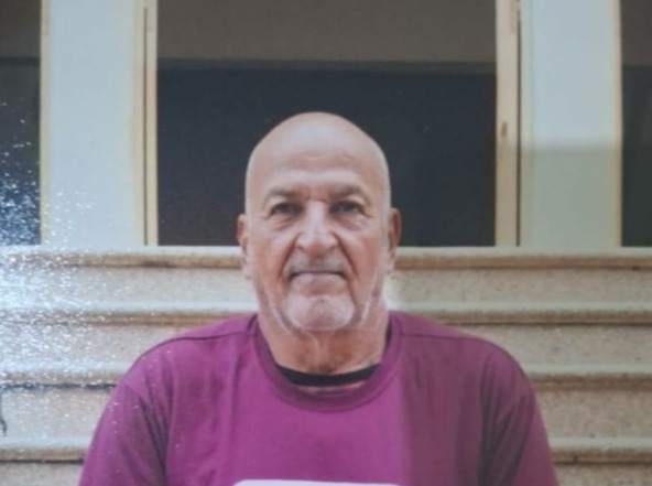 Raimundo: homem idoso, branco, calvo, de barba e bigode grisalhos e por fazer, olhos castanhos. Ele usa camisa rosa escuro e está em frente a uma escadaria bege.