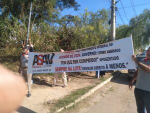 Dois homens idosos seguram uma faixa com a logo da Asav e os dizeres: "Greve pelo cumprimento integral do acordo de 2024. Governo: acordo assinado tem que ser cumprido! Aposentado sempre na luta! Nenhum direito a menos!".